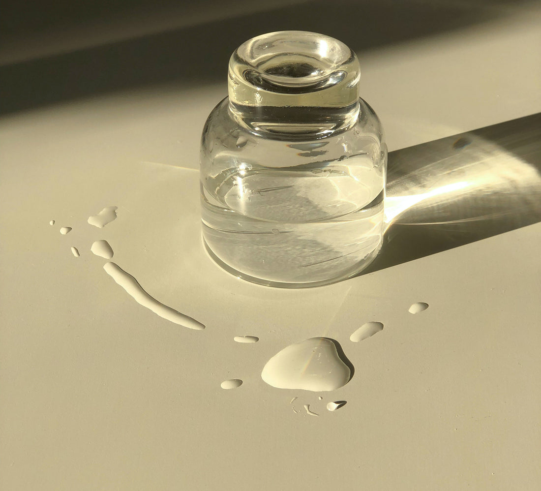 Gläschen mit klarer, viskoser Flüssigkeit und einigen Tropfen im Vordergrund als Symbolbild für Glycerin