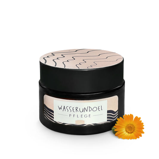 Tiegel mit milder Solecreme von wasserundoel mit kleiner Ringelblume im Vordergrund
