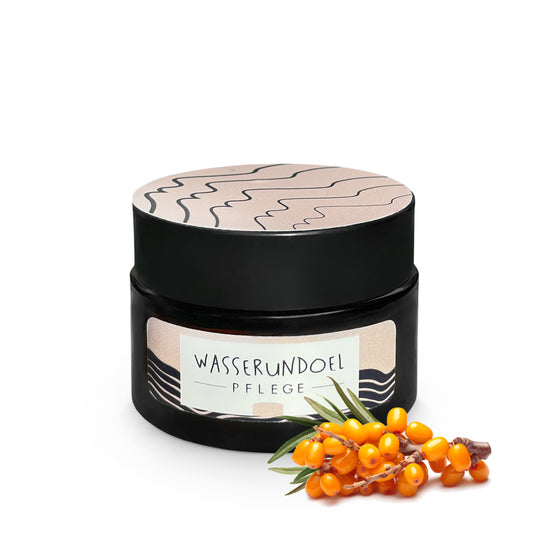 Tiegel mit Sanddorncreme von wasserundoel mit kleinem Zweig von Sanddornbeeren im Vordergrund